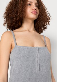 Camisola cinza de alças finas com riscas, apresentando um fecho de botões na frente e um tecido suave e texturizado.