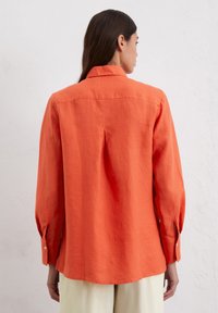 Camicia a maniche lunghe arancione brillante in lino, con piega sul retro e polsini con bottone, orlo dritto e vestibilità comoda.