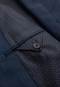 Gros plan d'une doublure de costume bleue à motifs avec une poche boutonnée et un tissu bleu texturé sur la veste extérieure.
