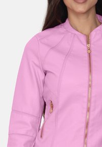Chaqueta de cuero lavanda con un diseño ajustado, cremallera dorada y bolsillos laterales. Textura suave con detalles de costura en los hombros.