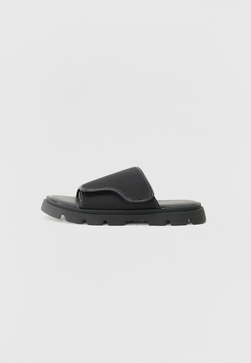 Black slide sandal with a wide upper strap, textured material, and a chunky sole featuring a patterned tread.