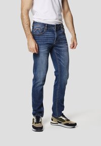 Blå denimjeans med lige ben, der har et klassisk fem-lomme-design og kontrastsyning, kombineret med sorte og beige sneakers.