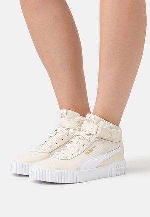 Baskets montantes beiges avec une semelle blanche et des accents. Matériau en cuir texturé avec une sangle velcro et un logo de marque bien en vue.