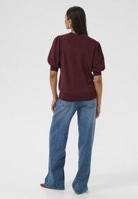 Vinröd stickad tröja med puffiga korta ärmar, ihop med högmidjade blå jeans. Slät textur, ribbade detaljer på ärmarna.