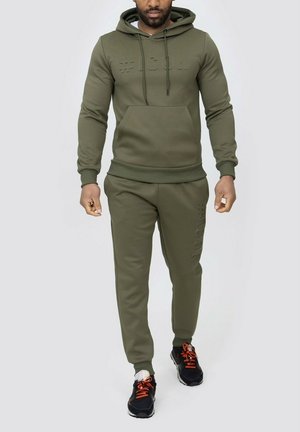 Ensemble de survêtement vert olive en tissu doux, comprenant un sweatshirt à capuche avec un logo texturé et un pantalon assorti avec des accents sur les côtés.