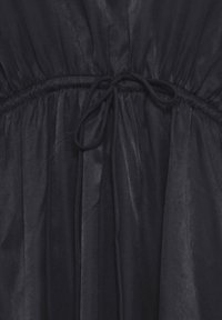 Sort stof med samlet elastisk søm og bundet snøre detalje i midten af taljen.