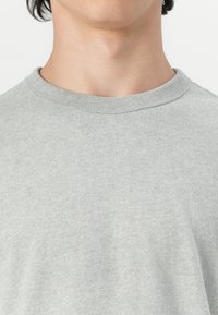 Lys grå t-shirt med rund hals, lavet af blødt stof, der har en glat overflade og minimal sømdetalje omkring kraven.