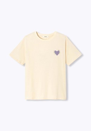 T-shirt beige à manches courtes avec encolure ronde et petit motif de cœur violet sur le côté gauche de la poitrine entouré de texte.