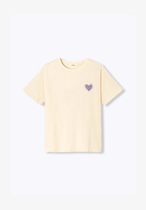 T-shirt beige à manches courtes avec encolure ronde et petit motif de cœur violet sur le côté gauche de la poitrine entouré de texte.