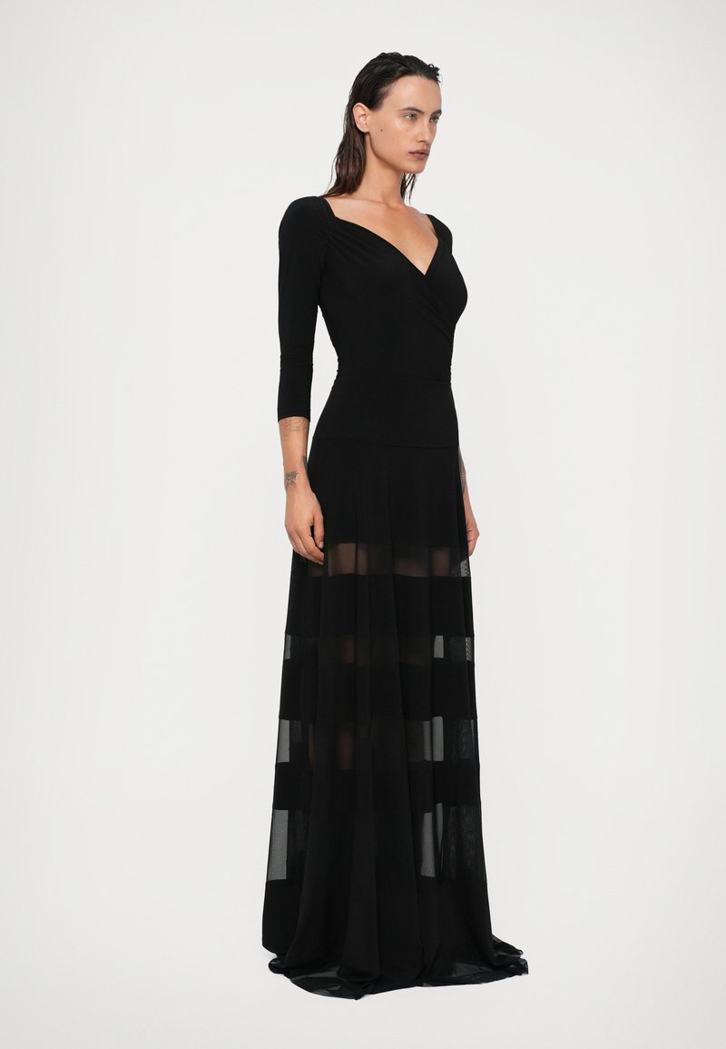 Black long dress with a fitted bodice and three-quarter sleeves. Sheer striped fabric at the skirt adds texture and depth. V-neck design.