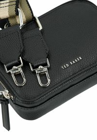 Schwarze, strukturierte Leder-Umhängetasche mit zwei silbernen Clipverschlüssen, einem Reißverschluss und einem Markenlogo auf der Vorderseite. Verstellbarer Riemen inklusive.