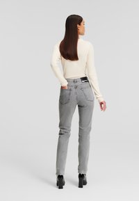 Grå denimjeans med en klassisk passform, raka ben, två bakfickor och en svart etikett vid midjan, tillsammans med en krämfärgad tröja.