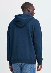 Felpa con cappuccio blu navy dalla vestibilità comoda. Tessuto morbido. Polsini e orlo a costine. Presenta un cappuccio foderato. Indossata con jeans azzurri.
