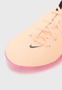 Nike boty s růžovou podrážkou a hladkým broskvovým svrškem, mají ploché tkaničky a malé černé logo na boku. Kulatý design špičky.