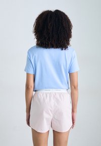 Světle modrá košile s krátkým rukávem v kombinaci s růžovými šortkami se bílým pasem Calvin Klein. Měkké materiály a uvolněný střih.
