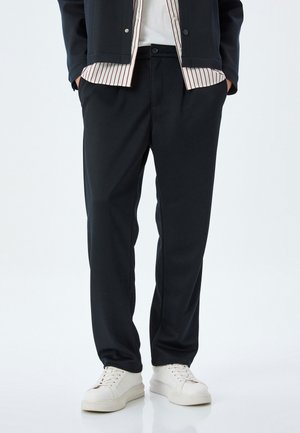 Schwarze Hose aus einem glatten Material mit geradem Bein, ausgestattet mit einem vorderen Knopfverschluss und tiefen Seitentaschen.