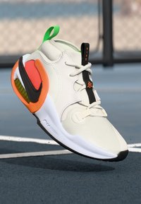 Hvid sneakers med mesh-overdel, distinkte orange og grønne accenter, sort snørresystem, polstret krave og en tekstureret sort sål.