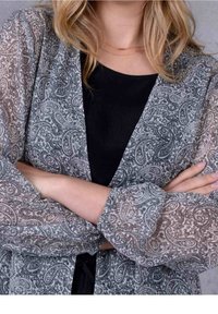 Průsvitné šedé kimono s paisley vzorem, dlouhými rukávy a otevřeným předním dílem, pod kterým je vidět černý vnitřní top s detailními květinovými motivy.