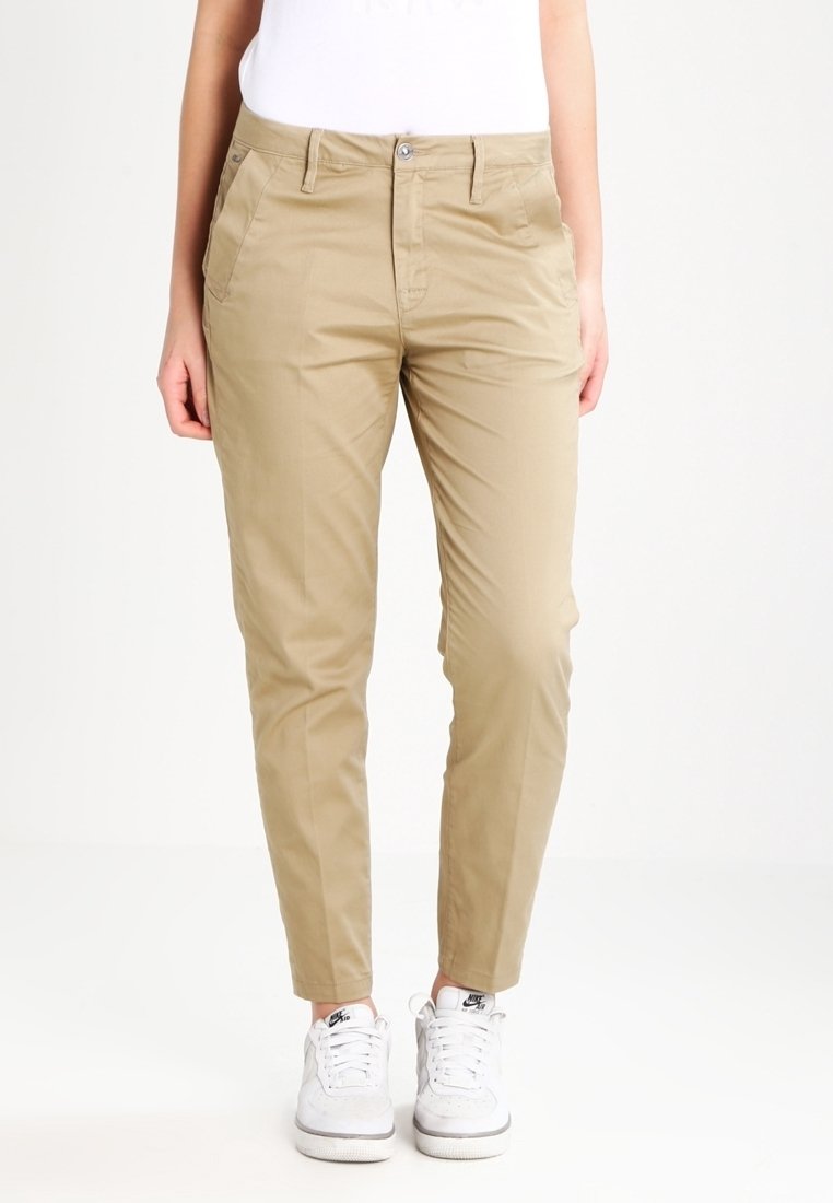 Khaki chinos, jotka ovat kapeammassa mitassa, litteällä etuosalla, etutaskuilla, vyölenkeillä ja yhdessä nappikiinnityksellä. Yhdistetty valkoisiin tennareihin.