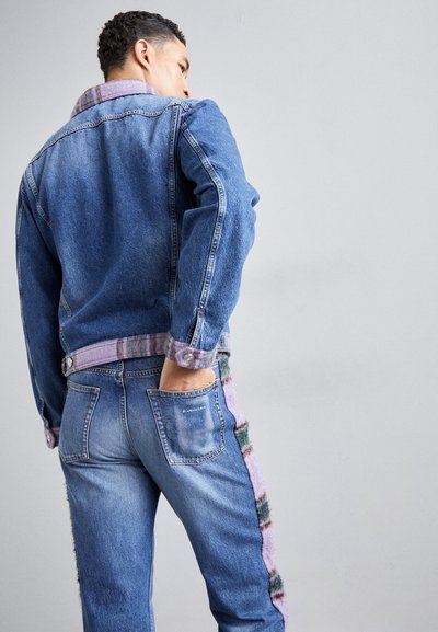 Veste en denim avec col et poignets en tartan, associée à un pantalon en denim avec des accents latéraux texturés dans des tons violets et verts.