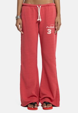 Pantaloni lounge rossi a gamba larga con coulisse bianca, ricamo "Jaded 3" sulla coscia sinistra, indossati con sandali neri e rossi.