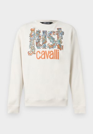 Biela mikina s dlhým rukávom s kvetinovými zdobenými písmenami, ktoré tvorí slovo "JUST" v modrej a oranžovej farbe nad výrazným nápisom "cavalli" v oranžovej farbe.