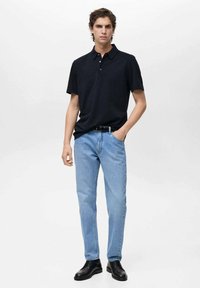 Čierna polo košeľa, svetlomodré džínsy, čierny opasok a čierne topánky. Jednoduchý dizajn, krátke rukávy a voľný strih. Žiadne viditeľné vzory.