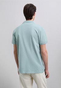 Tricou polo bleu deschis, cu croială lejeră, mâneci scurte și țesătură texturată. Are guler plat și tăieturi laterale la tiv.