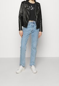 Schwarze Leder-Bikerjacke, verkürztes schwarzes T-Shirt, hellblaue Jeans und weiße Sneaker. Glatte Texturen, lässiges Design und taillierte Form.