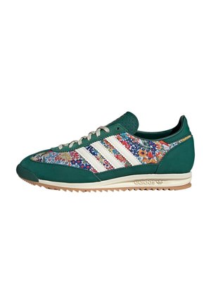 Groen-witte lage sneaker met bloemenstofpanelen, witte veters, witte strepen aan de zijkanten en een beige rubberen zool met ribbels.