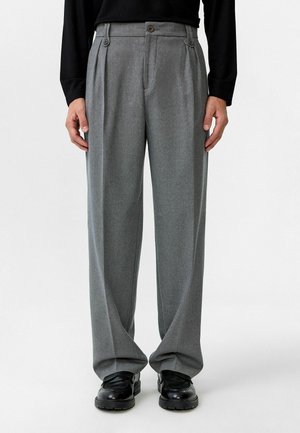 Grijze geplooide broek met een getailleerde pasvorm, voorzien van twee voorste knopen, een lichte textuur en een brede pijpdesign, gecombineerd met zwarte schoenen.
