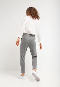 Graue Jogginghosen mit elastischem Bund, seitlichen Taschen und schmal zulaufendem Bein. Kombiniert mit einem weißen Langarmshirt und weißen Sneakers.