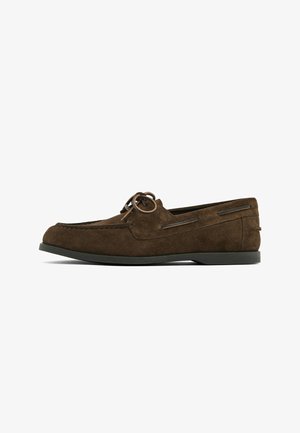 Mocassino in suede marrone con punta rotonda, dettagli in pizzo e accenti laterali discreti. Materiale testurizzato e suola in gomma a contrasto.