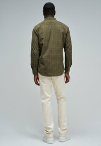 Koszula w kratę w kolorze oliwkowym z długimi rękawami, mankietami na guziki i zaokrąglonym wykończeniem, zestawiona z beżowymi spodniami slim-fit i białymi trampkami.