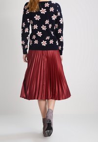 Navyblå tröja med rosa blommönster, kombinerad med en lång, plisserad bordeauxkjol och grå ankelboots. Texturerna är mjuka och släta.