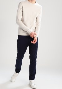 Maglione grigio chiaro a maniche lunghe con collo a giro abbinato a pantaloni blu navy e sneakers bianche. Il tessuto sembra liscio con una vestibilità casual.