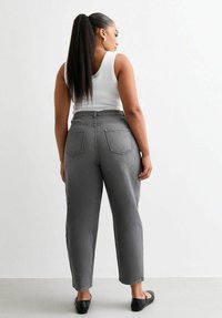 Jeans grises de tiro alto con un corte ligeramente holgado, que cuentan con dos bolsillos traseros y una tela texturizada. Se combinan con una camiseta sin mangas blanca y zapatos planos negros.