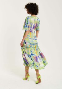 A colorful, patterned dress features short flutter sleeves, a flowing design in green, yellow, and blue, paired with bright green high heels.