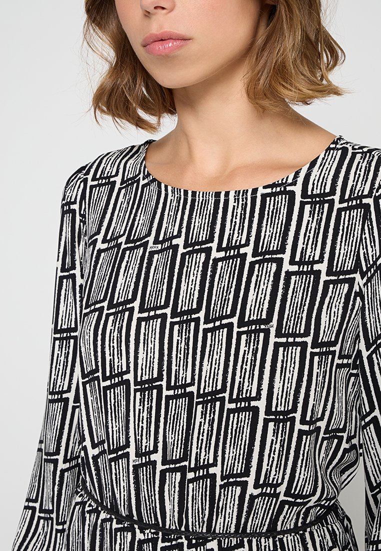 Vestido de estampado en blanco y negro con escote redondeado, que presenta un diseño lineal y una tela texturizada. Manga larga con cintura ajustada.