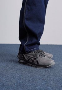 Gray athletic shoes with a textured pattern and black accents, worn with dark blue jeans featuring light stitching details.