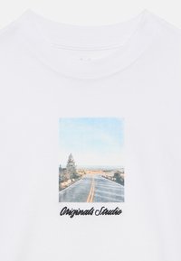 Λευκό μπλουζάκι με τετράγωνο γραφικό που απεικονίζει έναν γραφικό δρόμο με δέντρα, γαλάζιο ουρανό και το κείμενο «Originals Studio» σε μαύρη γραφή με καλλιγραφικά γράμματα.