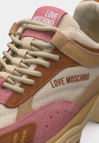 Πολύχρωνο αθλητικό παπούτσι Love Moschino με μπεζ κορδόνια, πάνελ από δίχτυ και σουέντ σε ροζ, καφέ και μπεζ, με λογότυπο κείμενο στη γλώσσα και στο πλάι.