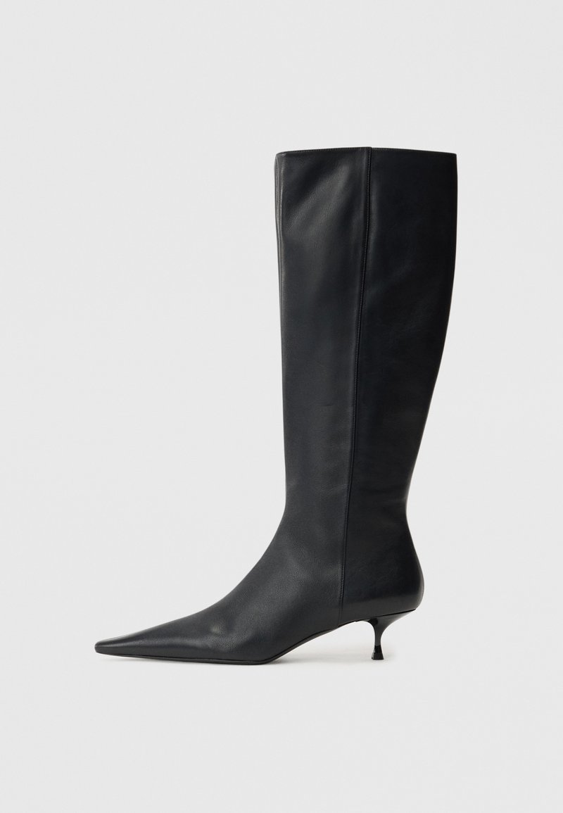 Black leather knee-high boot with a pointed toe and a tapered kitten heel. Smooth texture and minimalistic design with no visible hardware.