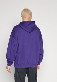 Felpa con cappuccio viola dalla vestibilità comoda, con grande cappuccio e polsini a coste. Texture liscia, con un design semplice senza grafiche o motivi.