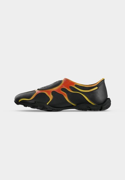 Μαύρο παπούτσι slip-on με πορτοκαλί και κίτρινα μοτίβα φλόγας, υφασμένο πέλμα και στρογγυλεμένη μύτη, απεικονίζεται σε προφίλ από το πλάι σε λευκό φόντο.