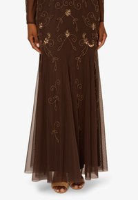 Hnědý večerní šaty s jemnou zlatou květinovou výšivkou, splývavou průsvitnou vrstvou a přiléhavým střihem s předním rozparkem.