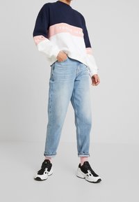 Sudadera a bloques de color en azul marino, rosa y blanco con el texto "TOMMY JEANS"; combinada con jeans holgados de color azul claro y zapatillas en blanco y negro.