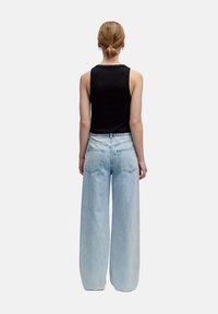 Zwarte mouwloze top gecombineerd met lichtblauwe wijdvallende jeans met hoge taille, twee achterzakken en subtiele vervaging in de denim.