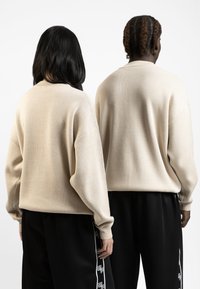 Beige gebreide truien met een oversized pasvorm, geribbelde manchetten en verlaagde schouders gecombineerd met zwarte joggingsbroeken met zijsstrips.