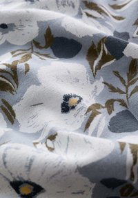 Tissu bleu clair avec un motif floral comprenant des fleurs blanches, des accents navy et des feuilles vert olive. Surface texturée avec un tombé doux.